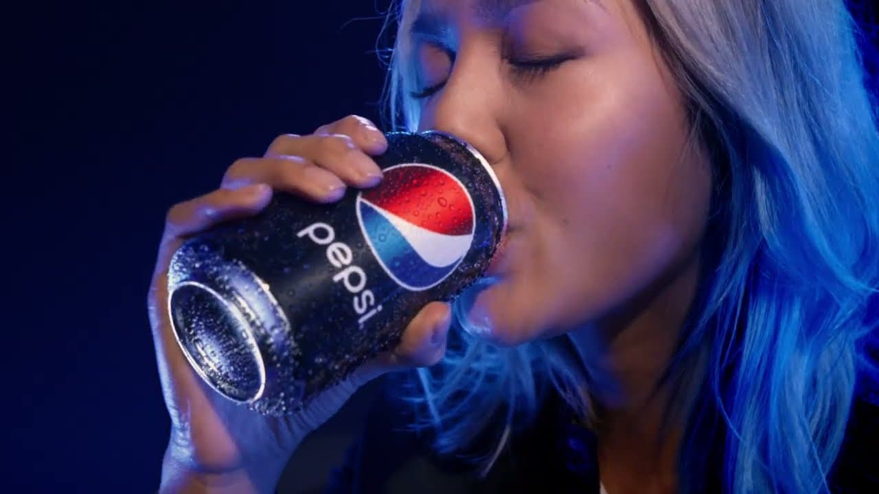 A close-up campaign image shows a woman drinking from a chilled Pepsi can under blue lighting.
